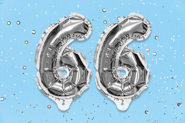 Silver foil balloon number, digit sixty six on a blue background with sequins. Birthday greeting card with inscription 66. Anniversary concept. Top view. Numerical digit. Celebration event, template.