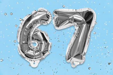 Silver foil balloon number, digit sixty seven on a blue background with sequins. Birthday greeting card with inscription 67. Top view. Numerical digit. Celebration event, template.