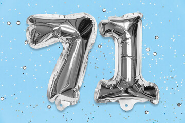 Silver foil balloon number, digit seventy one on a blue background with sequins. Birthday greeting card with inscription 71. Top view. Numerical digit. Celebration event, template.