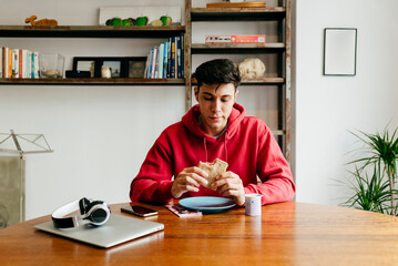 Young man having lunch and working on computer at home