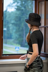 The girl is standing near the open window. Girl looking at the rain through an open window