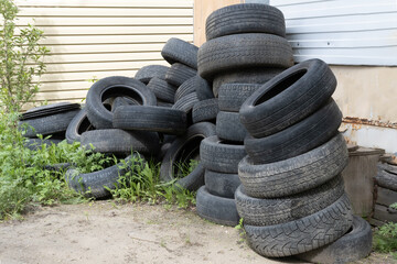 Old used wedge tires of cars and trucks are piled up and stored for recycling. Heap of many rubber tires wall background. Industrial pollution of the environment.