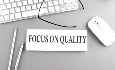 FOCUS ON QUALITY text on paper with keyboard on grey background