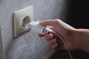 A young woman inserts a plug into a socket. A young woman plugs a charger or electrical appliance...