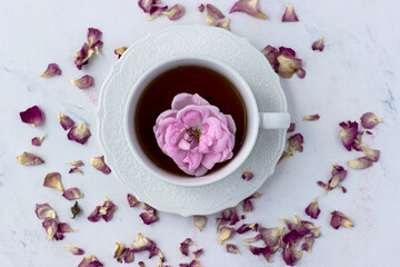 A cup of tea with a tea rose on a white marble background. Good morning. Top view