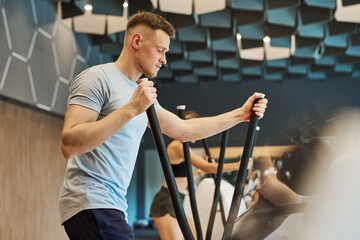 Young fitness man in sports clothing exercising on ellipsoid at the gym