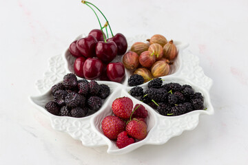Berry plate on a white background. Strawberries, gooseberries, cherries, raspberries and mulberries