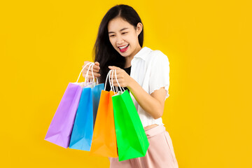 Young asian woman long hair style in black and white costume carrying the colorful paper shopping bags on yellow background.