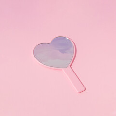 Valentines day creative layout heart shaped mirror with pink clouds reflection on  pastel baby background. 80s, 90s retro romantic aesthetic love concept. Minimal fashion idea.