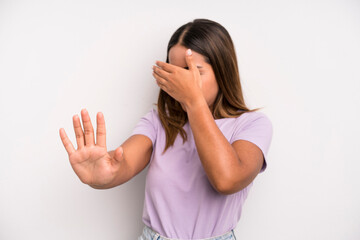 hispanic latin pretty woman covering face with hand and putting other hand up front to stop camera,...