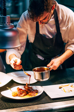 Professional chef pouring sauce on served meat