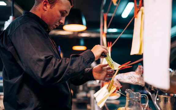 Man hanging papers with orders on kitchen