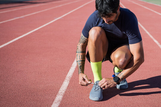 Ethnic sportsman tying laces on sneakers on track