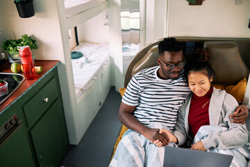 A multiracial couple watches a tv show in a motor home.