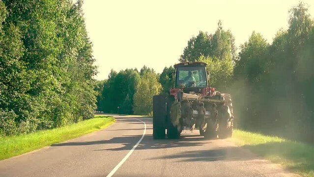 An agricultural tractor with a cultivator drives along the road along the forest