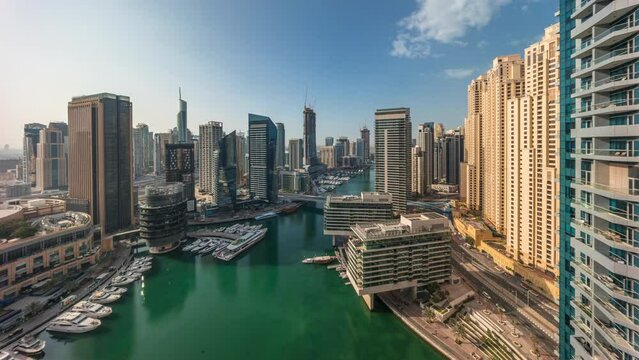 Aerial panoramic view to Dubai marina skyscrapers around canal with floating boats timelapse during sunrise. White boats are parked in yacht club