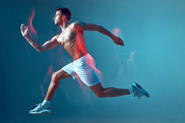 Running athletic male with naked torso in air on blue background in neon light. Motion blur. Modern guy athlete run