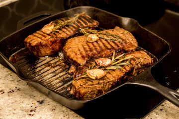 Grilling new york strip sirloin beef steaks with rosemary and garlic on cast iron grill pan skillet...