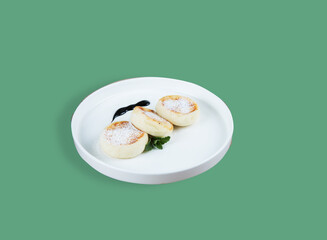 A white plate with morning breakfast - cottage cheese cakes on a green background.