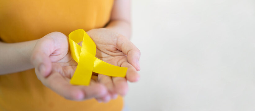 Young female holding yellow gold ribbon awareness symbol for endometriosis, suicide prevention, sarcoma bone cancer, bladder cancer, liver cancer and childhood cancer concept. Health care. Copy space.