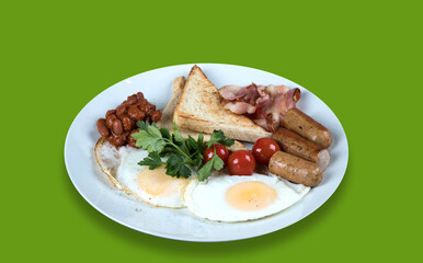 Side view of a plate with scrambled eggs, bacon, beans, sausages, tomatoes and croutons on a green background.