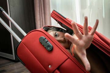 A child locked in a bag asks for help. The girl put her hand out of the red travel bag. The concept...