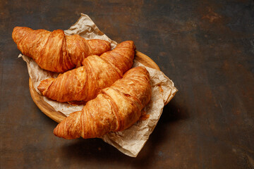 Crumpled bakery paper with tasty croissants on dark table, closeup. French pastry. Selective focus.