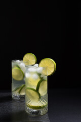 Dos vasos de refrescante zumo de lima con rodajas de lima y hielo sobre fondo negro