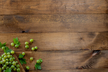 Wooden background. Green gooseberry with green leaves on a wooden board on a wooden background. Individual berries are scattered nearby. Place for text. Copy space.