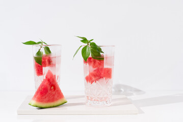 Dos vasos de zumo de sandía con trozos de sandia y hielo sobre fondo claro