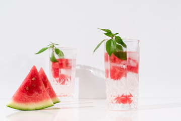 Dos vasos de zumo de sandía con trozos de sandia y hielo sobre fondo claro