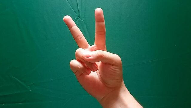 a man's hand forming a peace symbol on a green screen background