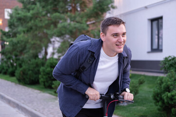 Obraz premium A businessman on an electric scooter rides through the park with a backpack. a man moves around the city on eco-friendly transport.