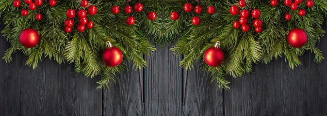 Christmas banner with spruce branches and red bead on the black wooden background. Copy space.