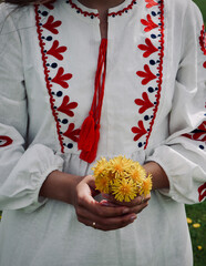 A young woman in a national Ukrainian costume, an embroidered shirt, holds a bouquet of yellow flowers.