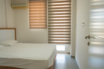 Interior of a bedroom in a hotel with a white bed and blinds on the windows