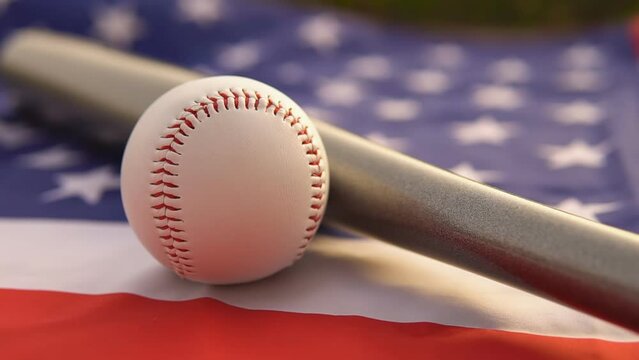 White leather ball and baseball bat laying on flag of the United States of America USA, close up