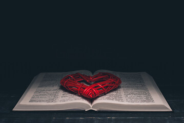 Open Bible. Red heart on the book. Holy Bible. On a black background.