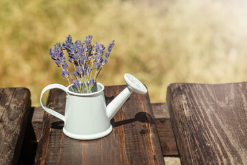 Bouquet of purple lavender flowers, in a white decorative watering can on a wooden background. Place for an inscription. Selective focus. © Nataliia