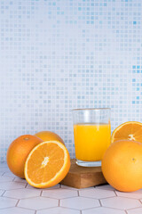 Glass of orange juice squeezed over a board and oranges around it.