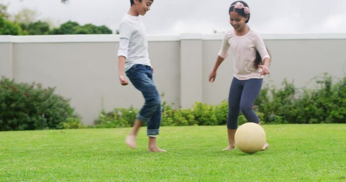 Happy soccer sport playing kids or child friends of boy and girl in family home backyard or outdoor house yard. Fun and young siblings or children bond and play football sports game with ball outside