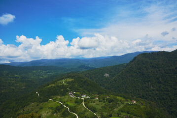 Mountains covered with green grass and trees, dirt roads and residential buildings.