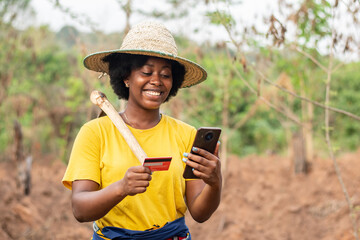 happy african farmer using her phone and credit card