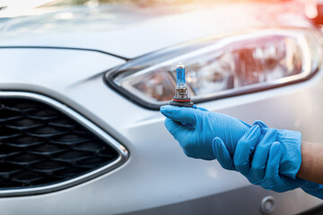Close-up photo of a man's hands holding a car light bulb near the car for replacement.