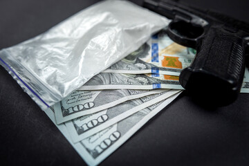 Cocaine in bags next to dollars and a gun isolated on black background.