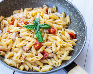 Italian pasta with swordfish, cherry tomatoes, oil and basil in a pan on a table Selective focue