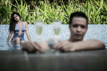 Woman with her boyfriend drinking champagne in the pool. Lovers in a hotel. Young couple bathing