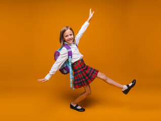 Cute happy schoolgirl in uniform walking on a yellow background. a child with a backpack. the...