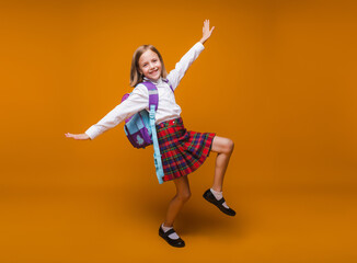 Cute happy schoolgirl in uniform walking on a yellow background. a child with a backpack. the little girl is ready for school. Dynamic images. back to school