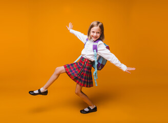 Fototapeta na wymiar Cute happy schoolgirl in uniform walking on a yellow background. a child with a backpack. the little girl is ready for school. Dynamic images. back to school